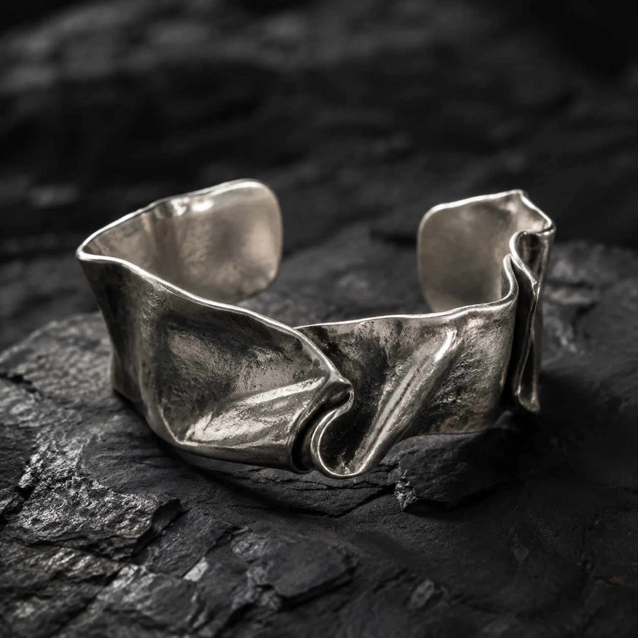 A sculptural silver cuff resting on dark stone